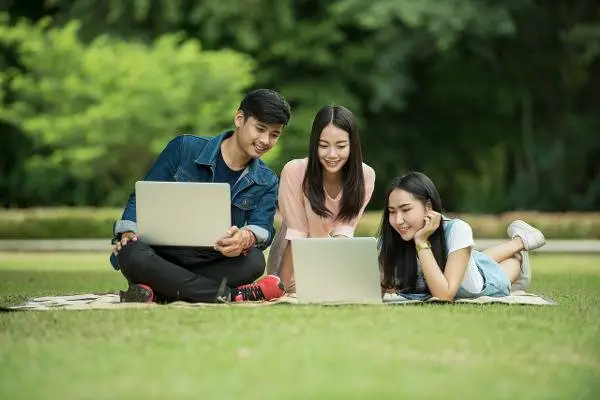 Teens studying on laptops at a park